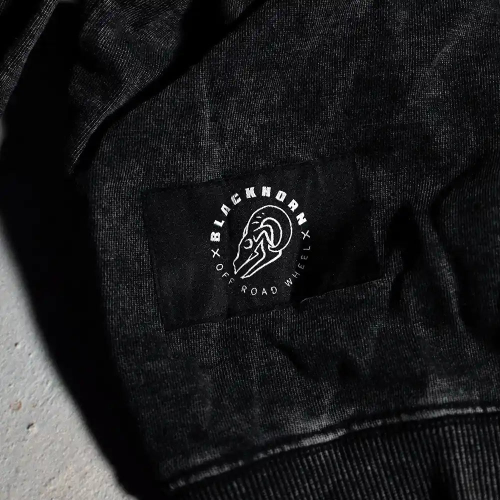 Close-up of the hem on the PAVEMENT ENDS Hoodie featuring Blackhorn Offroad woven label with Blackhorn skull logo and “Off Road Wheel” text on washed black fabric.