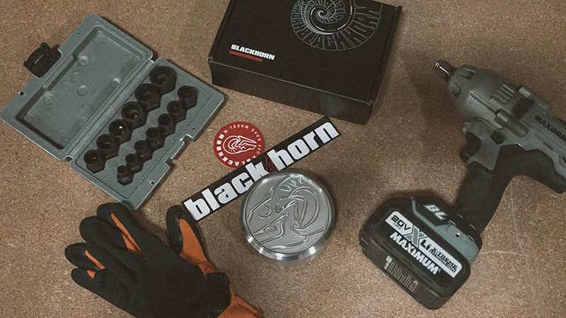 Labor Day themed Blackhorn Offroad flat lay with gloves, lug nut kit, power tool, wheel center cap, Blackhorn box, and stickers on workbench