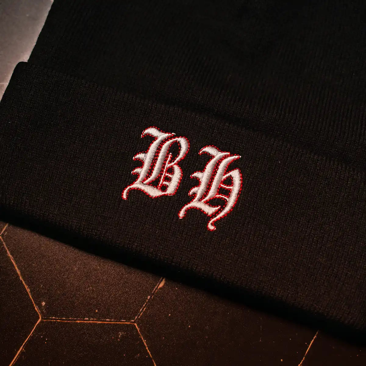 Close-up of white Blackletter logo embroidery with red outline on Blackhorn Offroad black knit beanie.