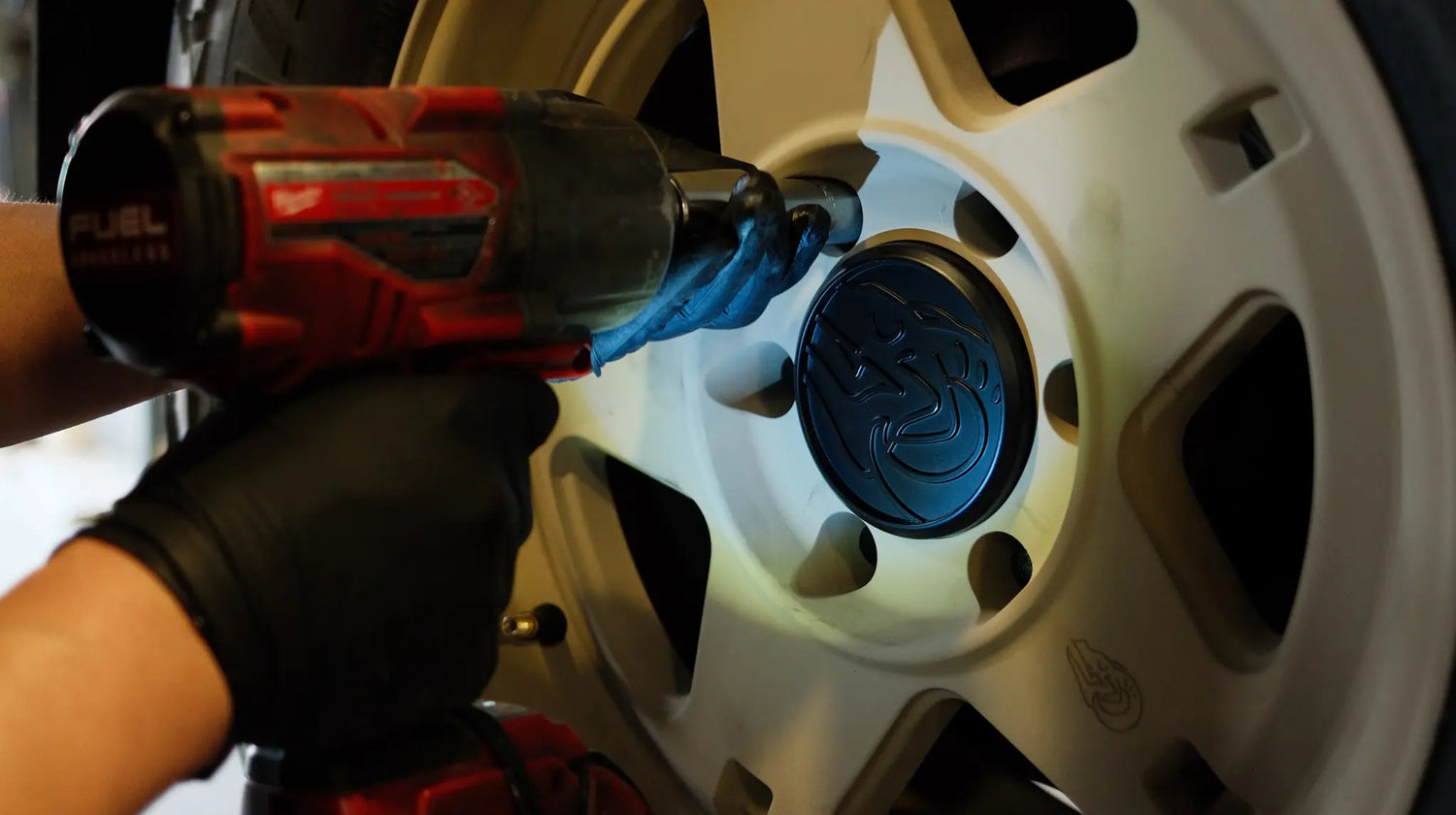 Technician using an impact gun to install the Blackhorn Offroad NS5 wheel in FDE finish, securing the lug nuts while showcasing the embossed Blackhorn Skull Strata Cap.