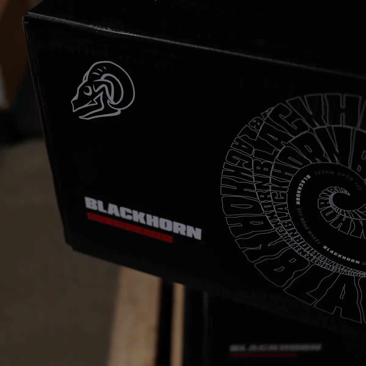Close-up of a Blackhorn Offroad wheel box on a pallet, captured in a dimly lit warehouse