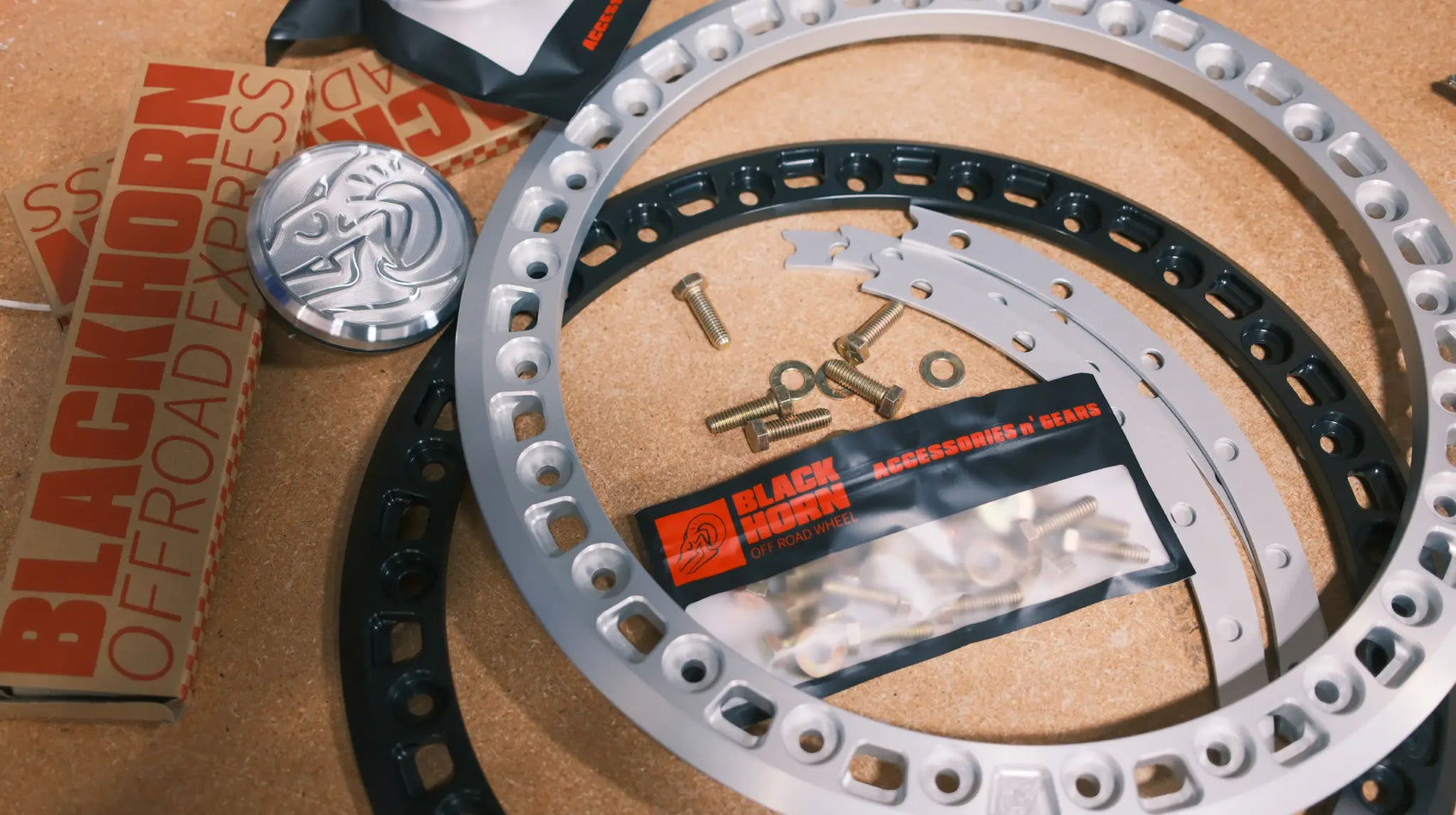 Blackhorn MBF beadlock system components laid out with rings, hardware kit, spacer, and center cap in anodized and black finishes